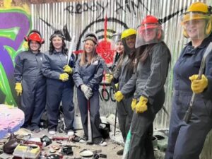 A group of rage room patrons line up inside for post-smash photo opportunity.