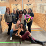 A group of women posing in front of axe-throwing tunnels at All Out Smash in Denver, Colorado