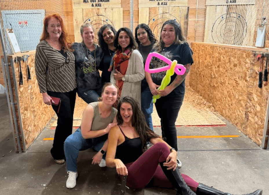 A group of women posing in front of axe-throwing tunnels at All Out Smash in Denver, Colorado