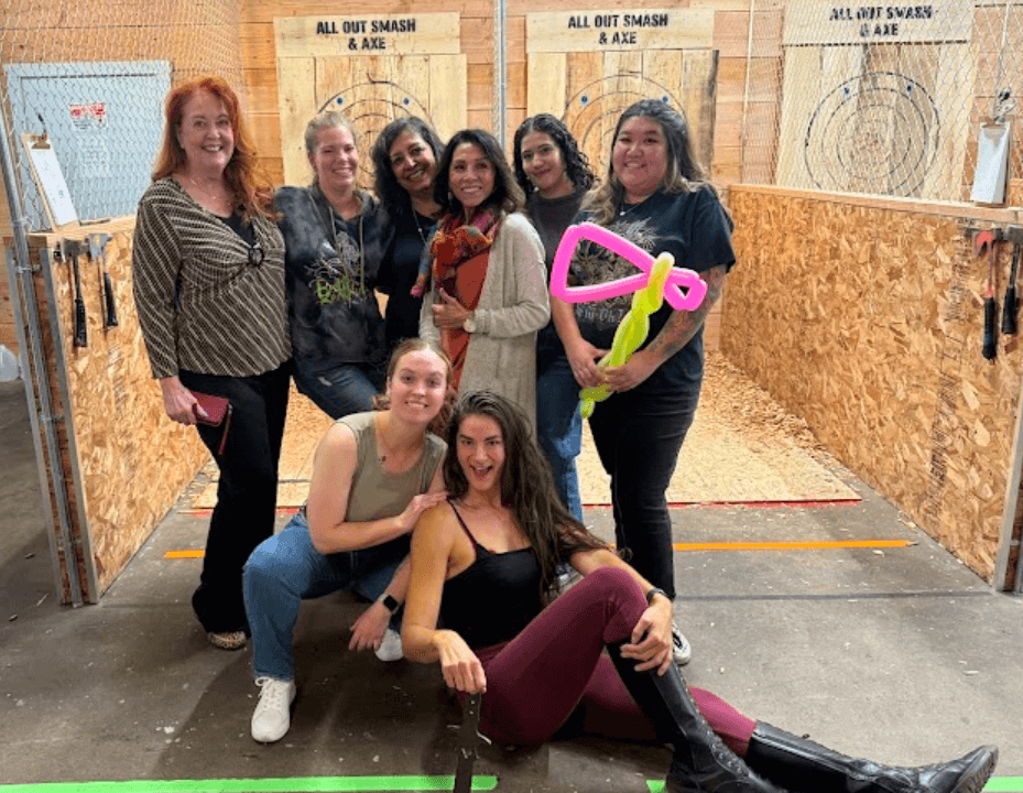 A group of women posing in front of axe-throwing tunnels at All Out Smash in Denver, Colorado